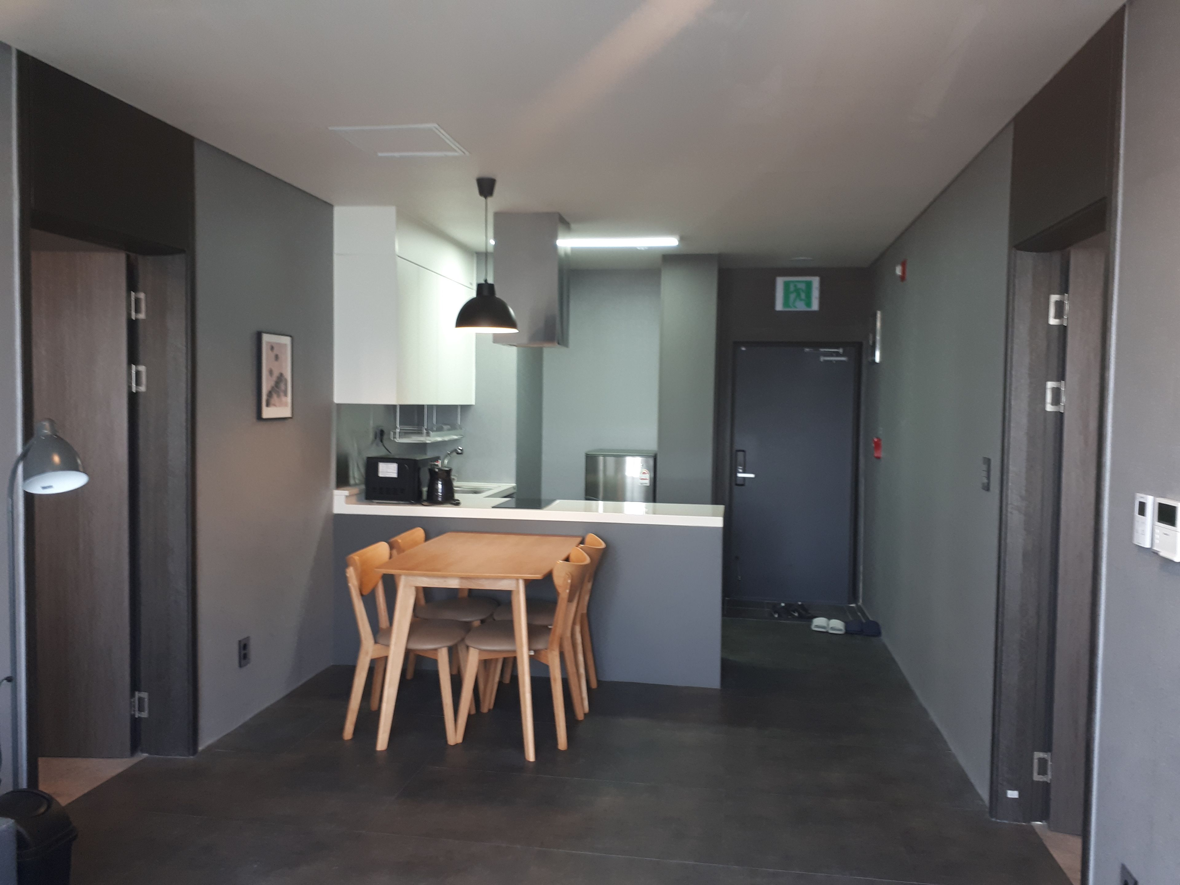 Una cocina moderna con una mesa y sillas de madera, una lámpara colgante y una puerta con letrero de salida.