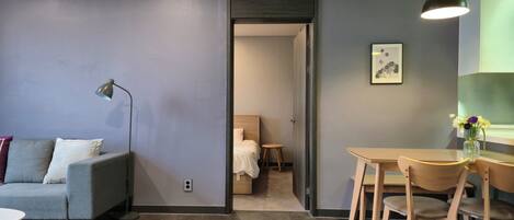 Quarto de hotel moderno com um sofá cinza, uma mesa redonda pequena e uma área de refeições com cadeiras de madeira.