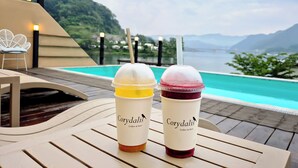 Deux grands verres de café glacé, chacun muni d’une paille, sont posés sur une table en bois, près d’une piscine, avec une vue sur les montagnes.
