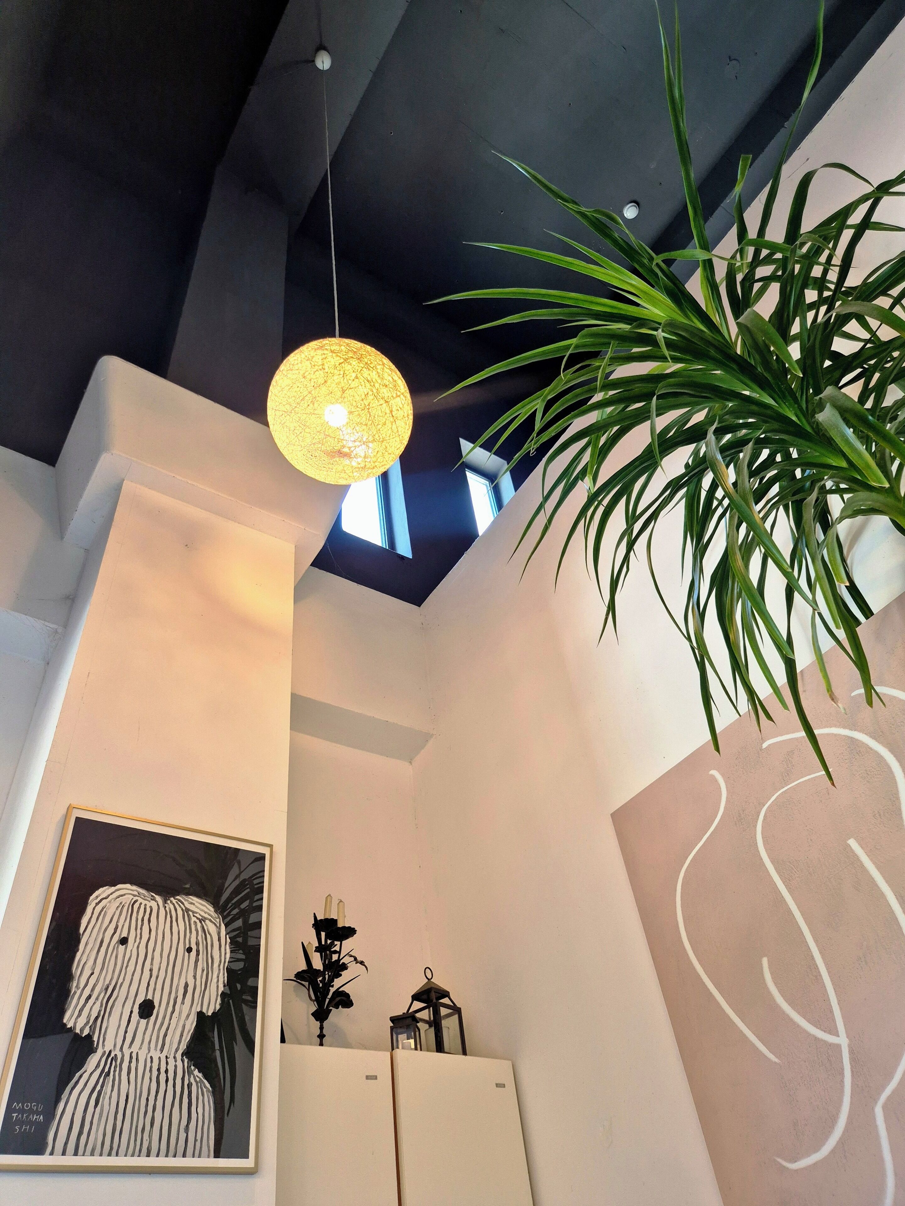 A modern interior with a hanging light fixture, a framed artwork, and a potted plant.