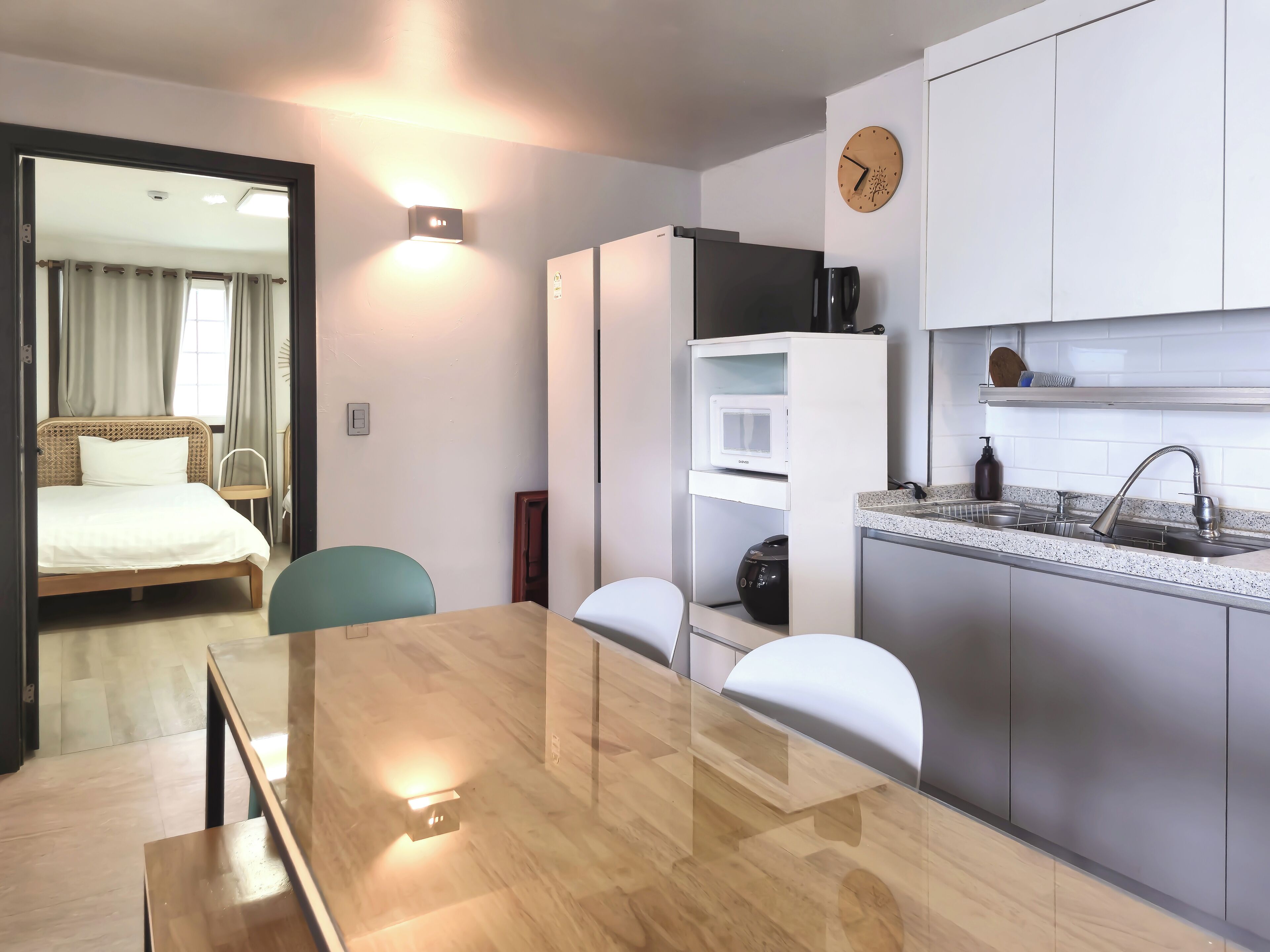 Quarto de hotel compacto com cama, mesa de cabeceira, cadeira, cozinha compacta e área de refeições com mesa e cadeiras.