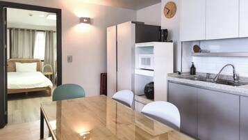 Quarto de hotel compacto com cama, mesa de cabeceira, cadeira, cozinha compacta e área de refeições com mesa e cadeiras.