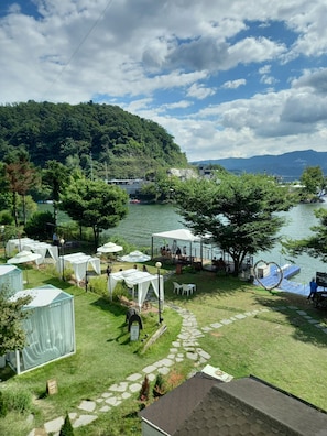 A lakeside campsite with tents, a covered seating area, and a heart-shaped decoration near the water. - Interlaken Pension in Gapyeong (Gapyeong)