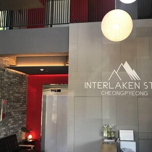 A modern interior with a reception desk, a wall-mounted sign for Interlaken St. Cheongpyeong, and a red accent wall. - Interlaken Pension in Gapyeong (Gapyeong)