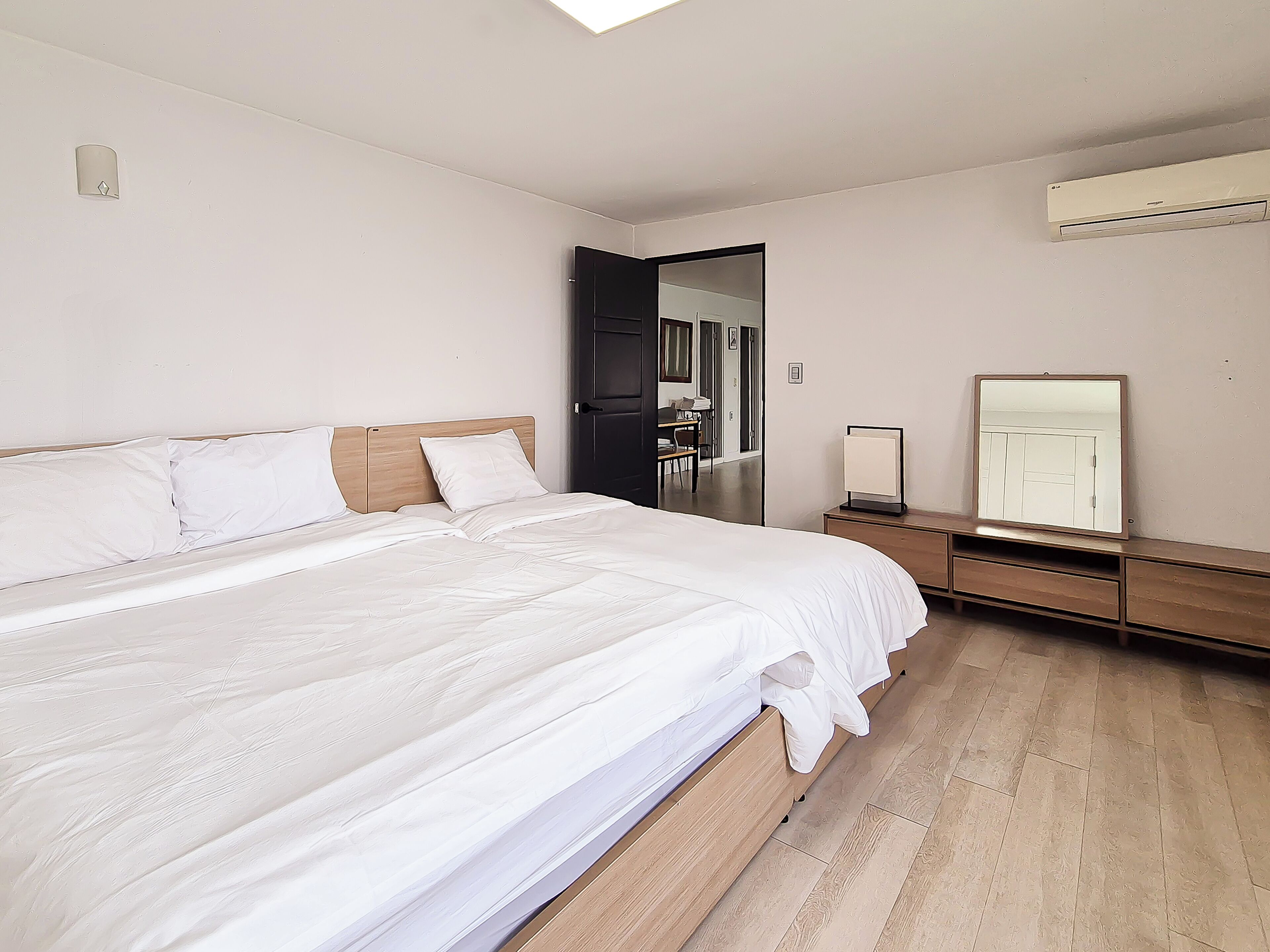 Un dormitorio con una cama grande, una mesita de noche, un espejo y un equipo de aire acondicionado.