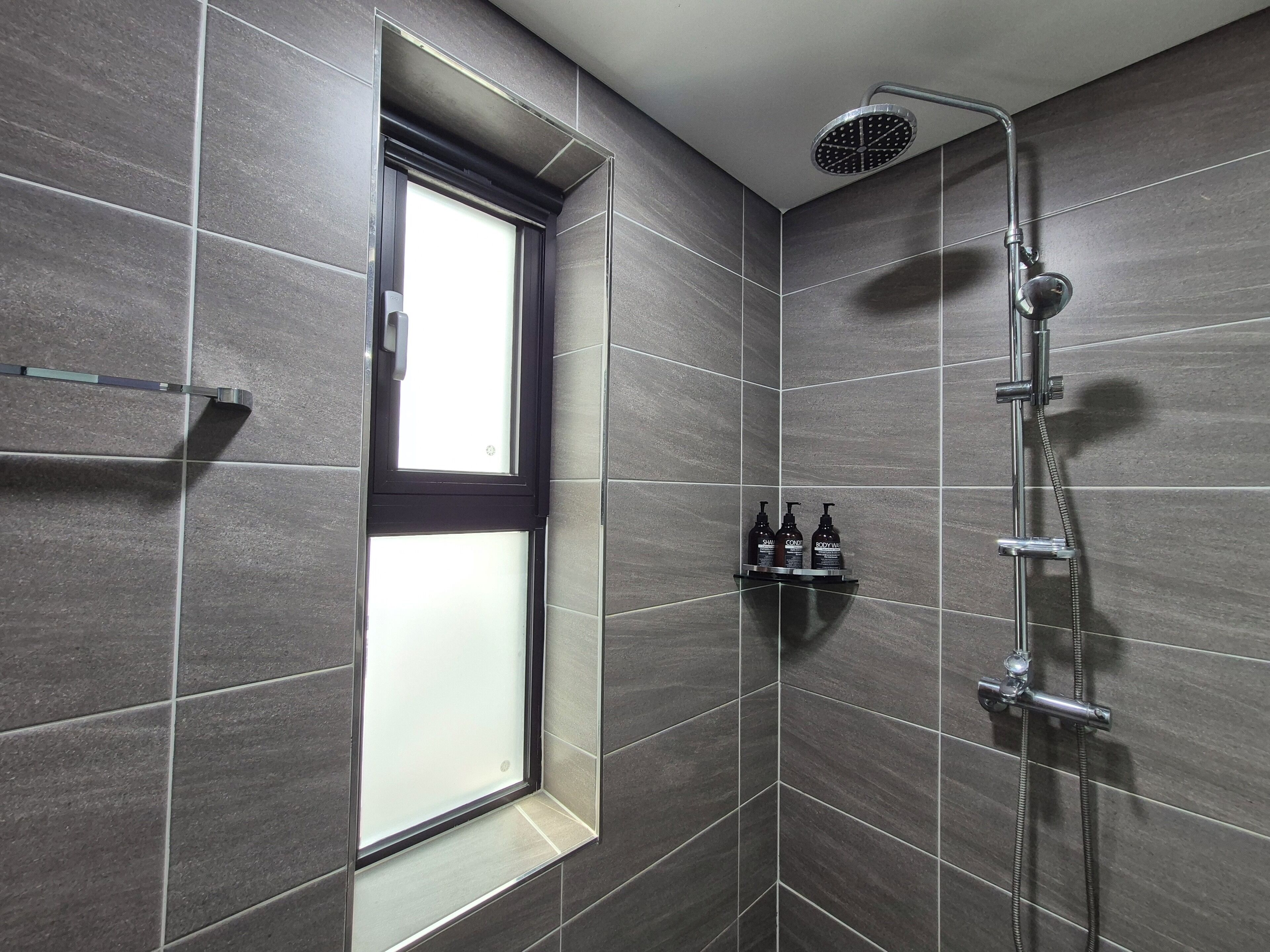 Ducha moderna con ducha de lluvia, una ventana y un estante con artículos de aseo.