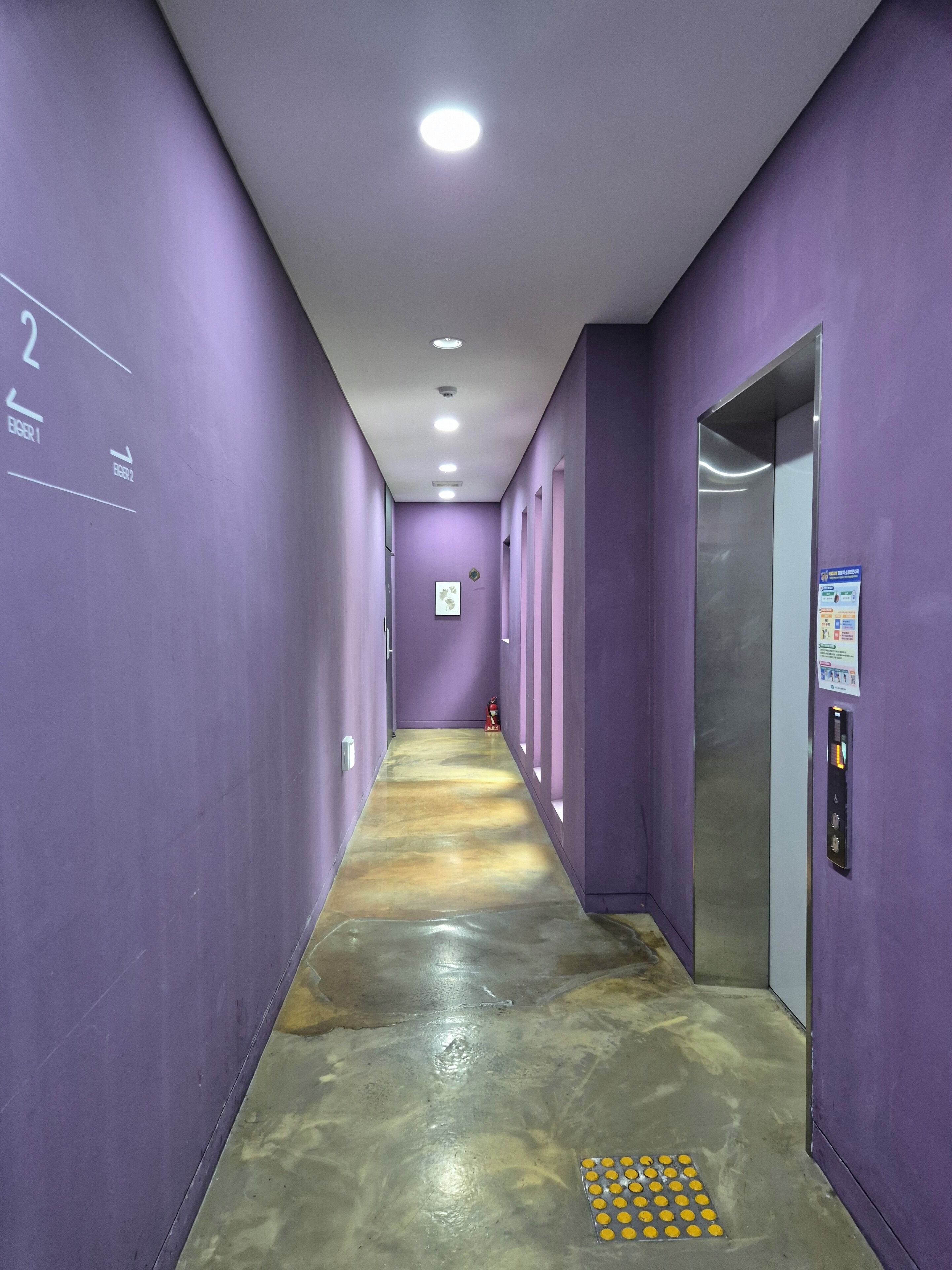 A hallway with purple walls, a shiny floor, and an elevator on the right.