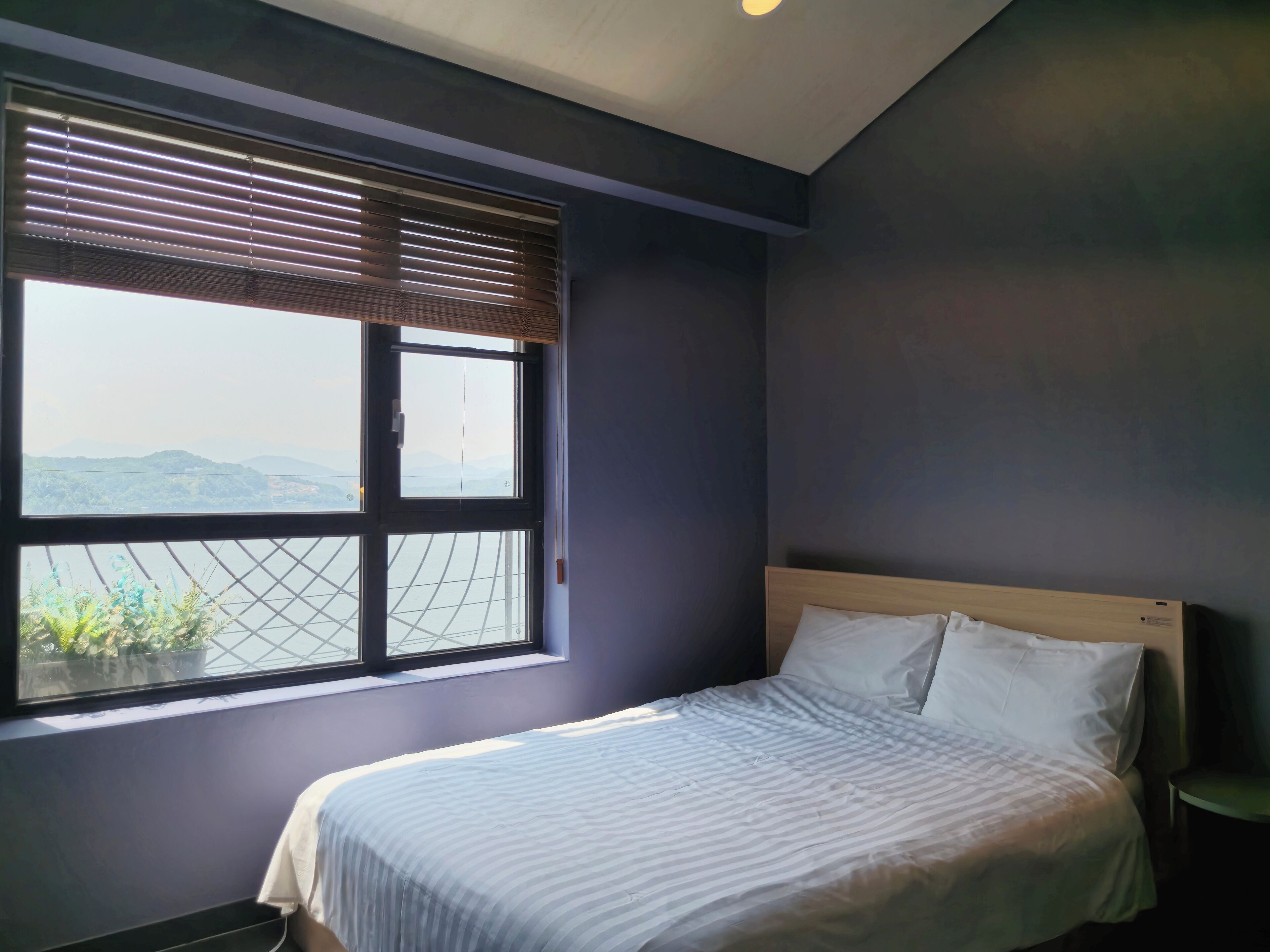 A bedroom with a bed, a window with blinds, and a view of mountains.