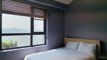 A bedroom with a bed, a window with blinds, and a view of mountains.