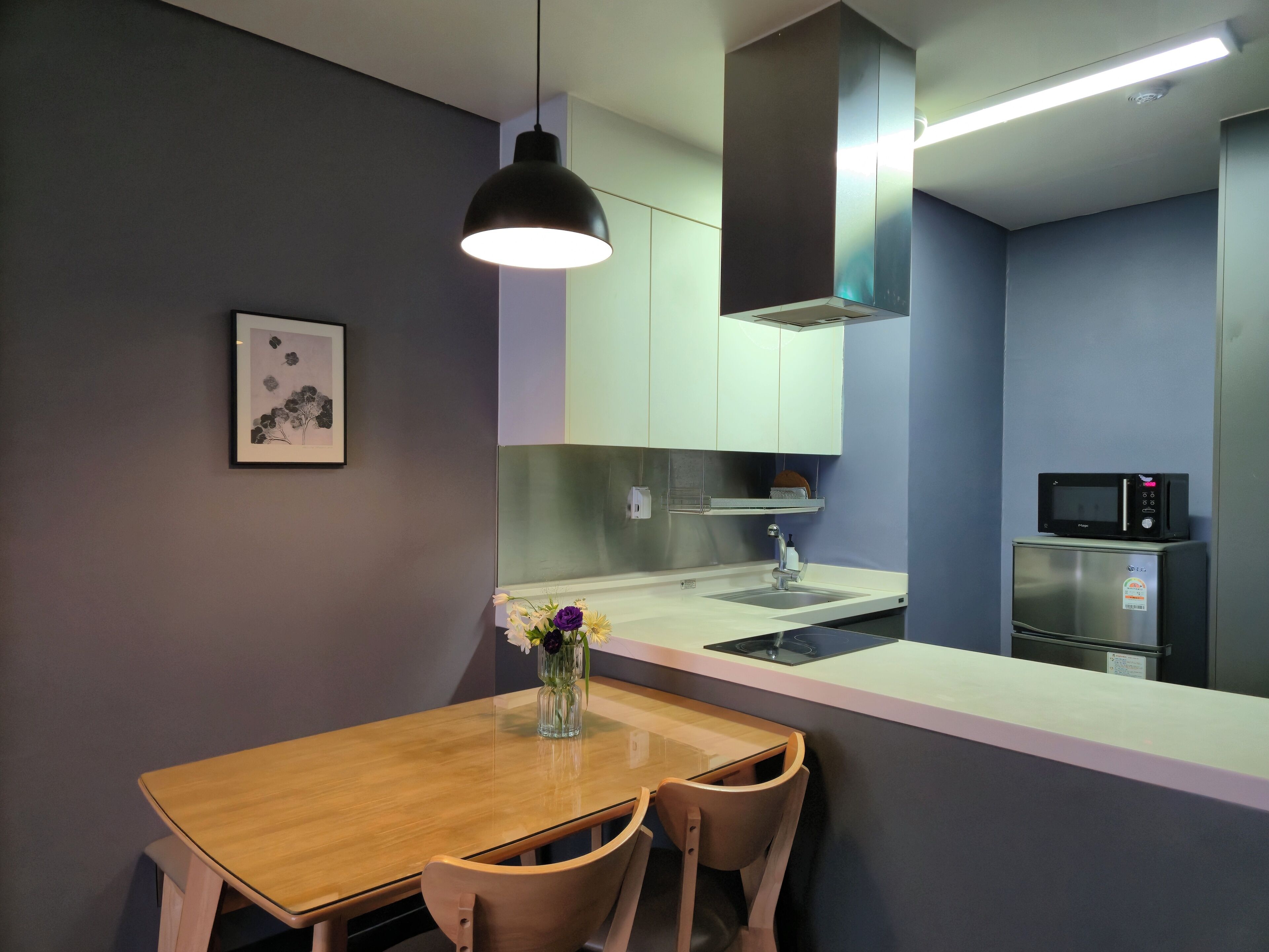 Una cocina moderna con una mesa de comedor de madera, dos sillas, una lámpara colgante, un microondas y un refrigerador.