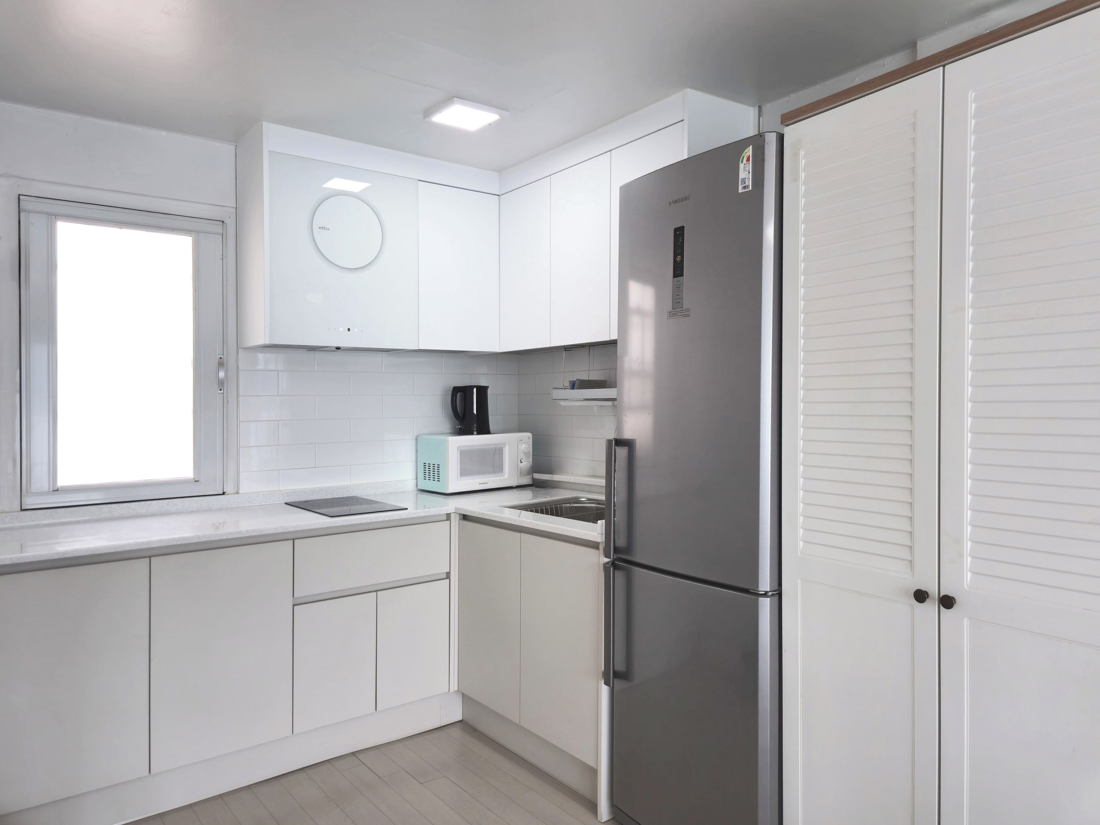 Una cocina moderna con armarios blancos, un refrigerador de acero inoxidable, un microondas y una cafetera.