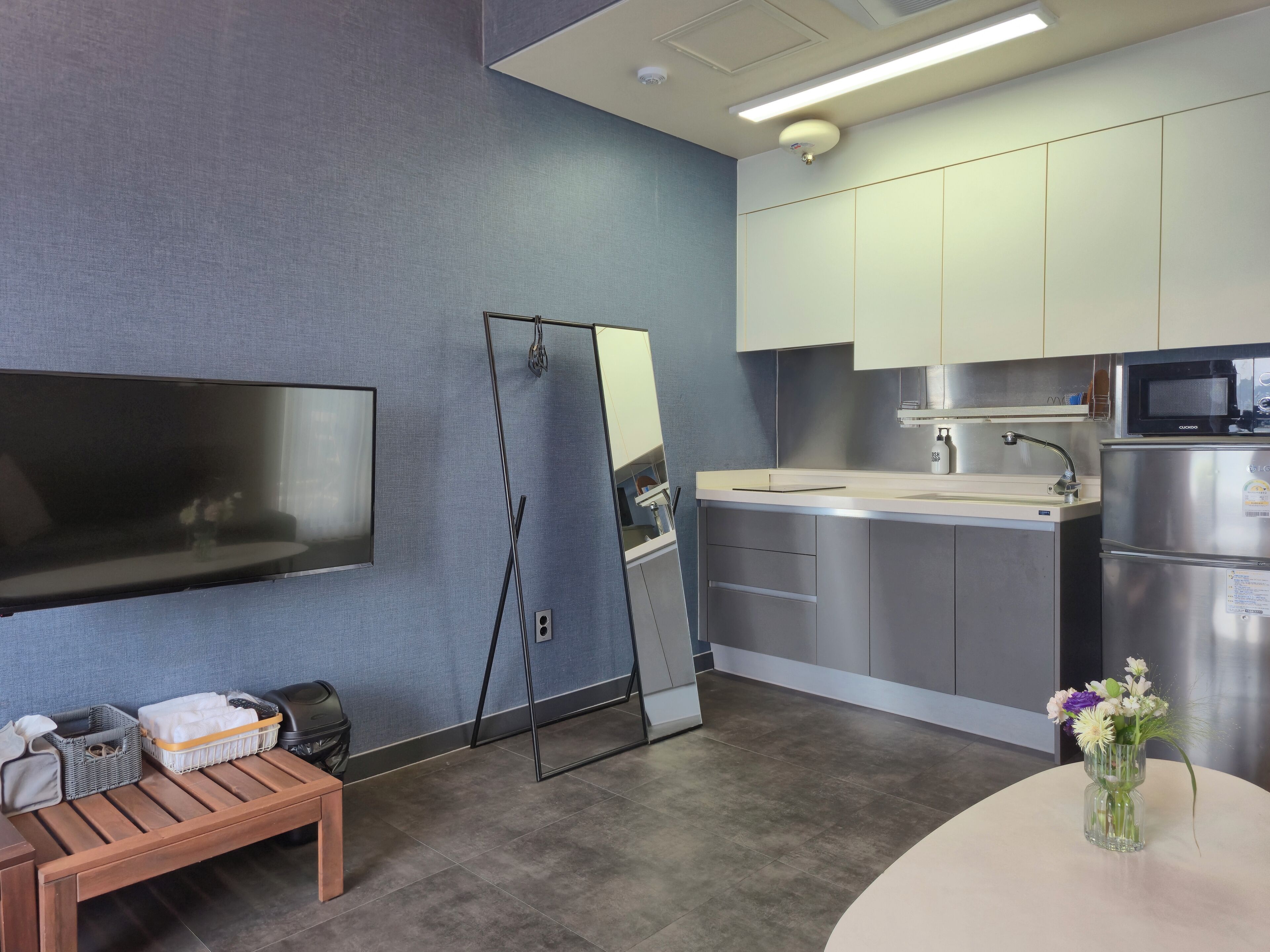 A modern kitchen with stainless steel appliances, a flat-screen TV, and a bench with storage baskets.