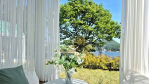 Une pièce avec vue sur un arbre et un plan d’eau. On y trouve une table sur laquelle est posé un vase de fleurs.