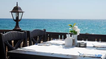 A table set for two with a view of the sea, a lantern, and a vase with flowers.