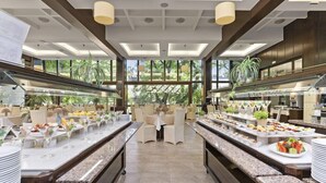 A modern buffet setup with multiple serving stations, glass railings, and a view of greenery outside. - Hotel Riviera Beach AND SPA (Golden Sands)