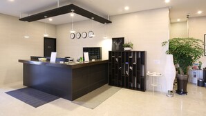 Un área de recepción moderna con un mostrador oscuro, un reloj digital y una planta en maceta.