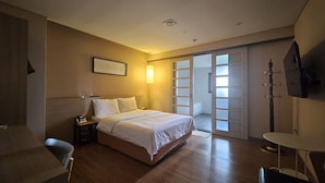 Habitación de hotel con cama, mesita de noche, lámpara y vistas al exterior por una puerta corredera.