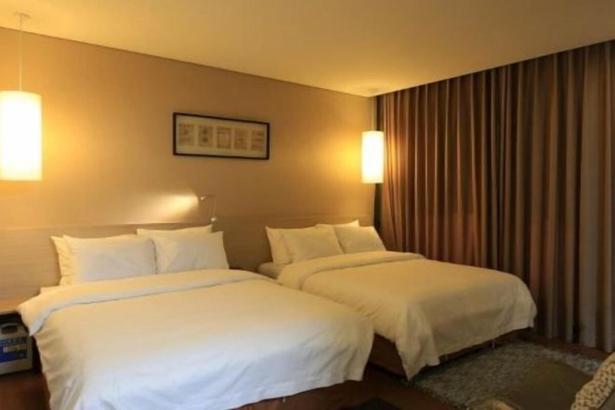 A hotel room with two beds, a nightstand, a lamp, a framed picture on the wall, and a curtain.