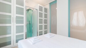Een hotelkamer met een bed, een badkamer met douche en een garderobe met ruitenverdeling.