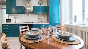 Een moderne keuken met blauwgroene kastjes, een houten eettafel gedekt met kommen en glazen, en een raam met uitzicht.