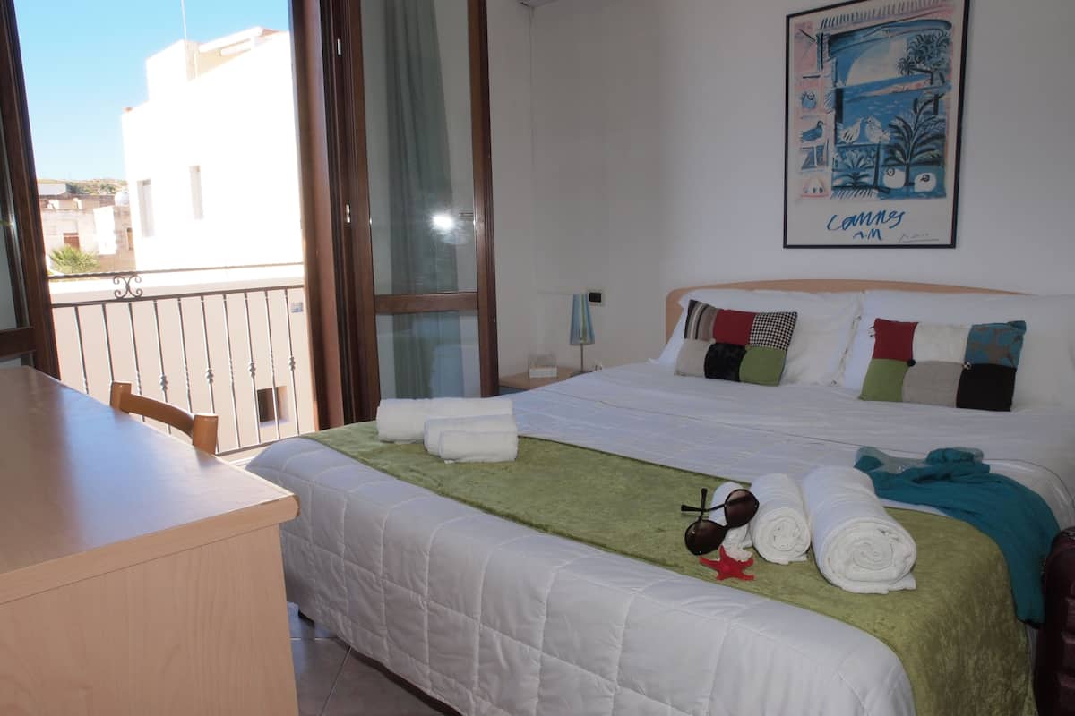 A hotel room with a bed, a desk, and a balcony.
