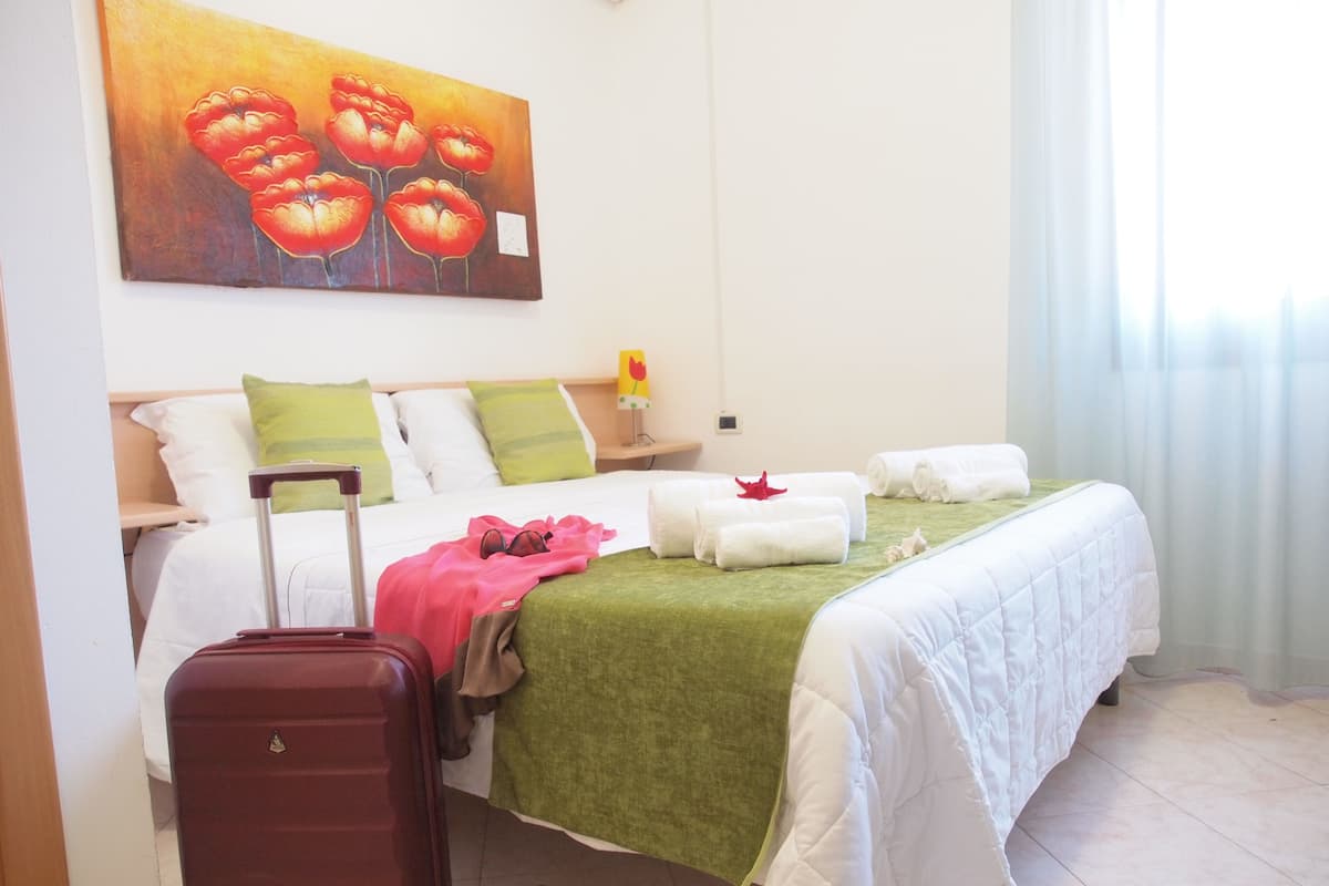 A hotel room with a bed, a suitcase, and a painting on the wall.