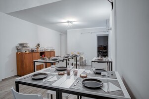 Zona pranzo moderna con diversi tavoli apparecchiati, un mobiletto in legno e una cucina sullo sfondo.