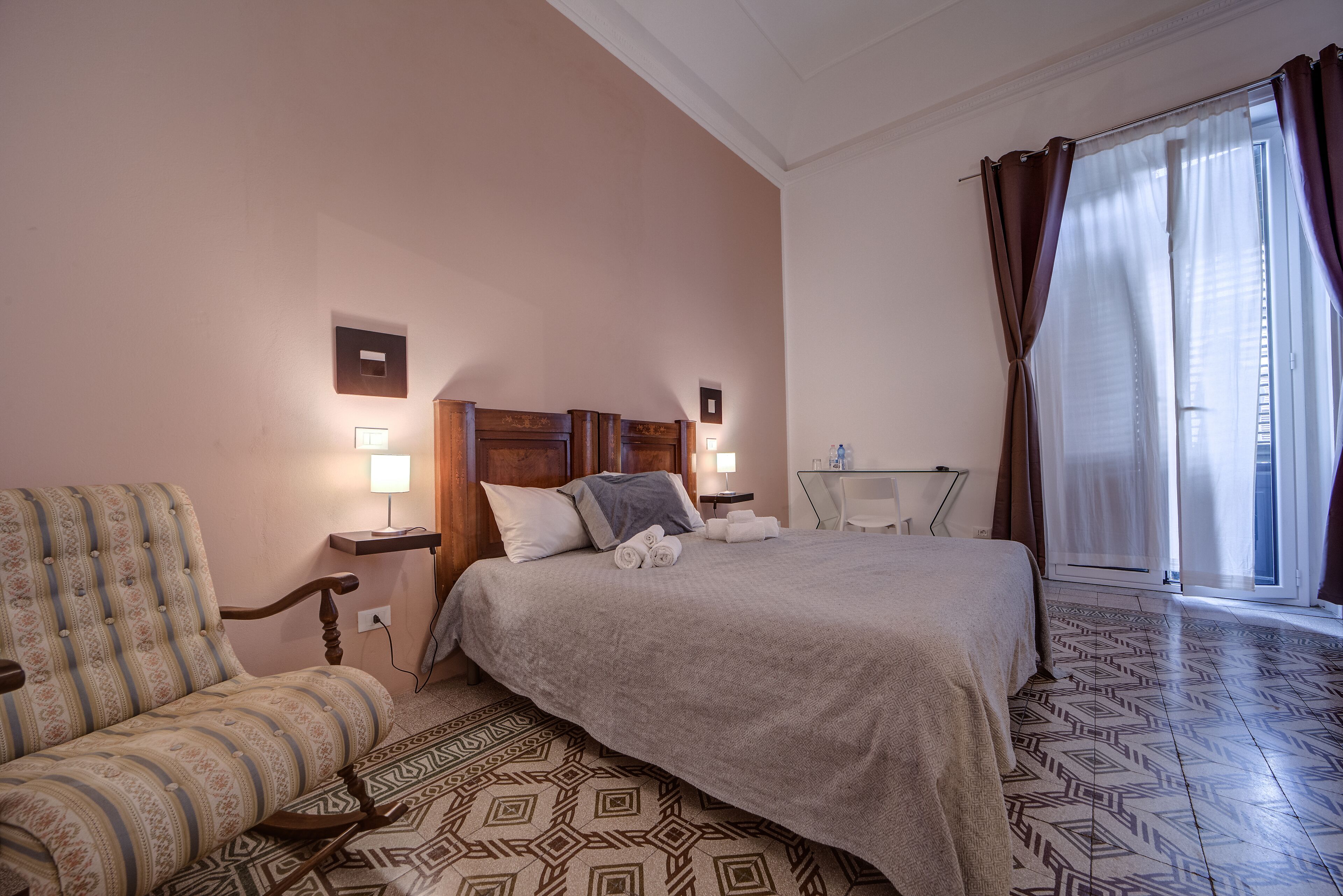 Habitación de hotel con cama, una silla, mesita de noche con lámpara y suelo estampado.