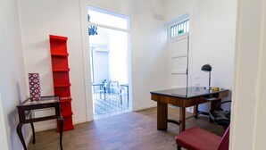 Une pièce avec un plancher en bois, une chaise rouge, un bureau avec une lampe et une étagère rouge.