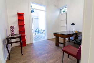 Una stanza con pavimento in legno, una sedia rossa, una scrivania con lampada e una libreria rossa.