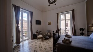 Une chambre d’hôtel avec un lit, une chaise, une petite table, une télévision et un balcon avec des rideaux.