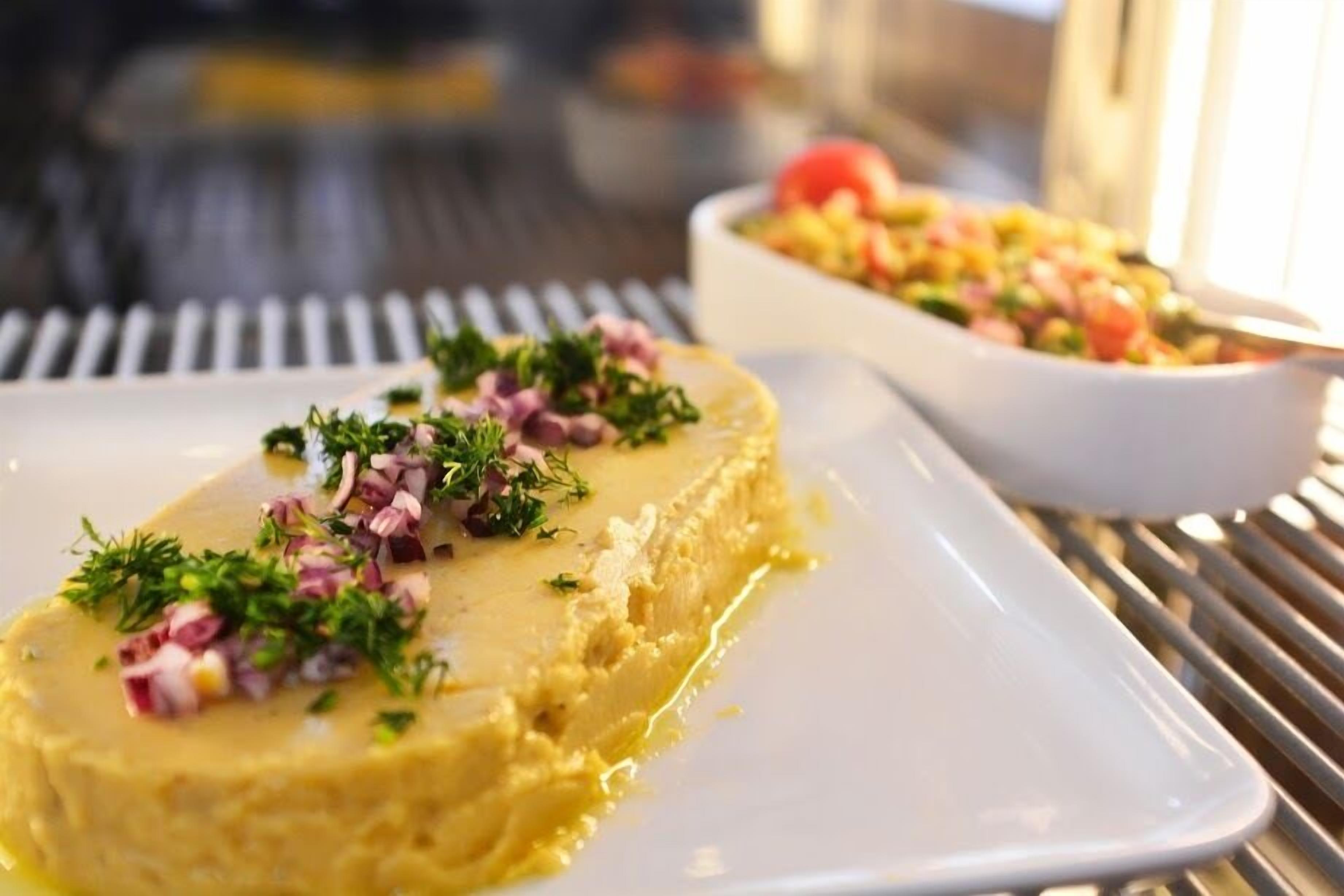 Un plat à la texture crémeuse, garni d’herbes et d’ingrédients coupés en dés, servi dans une assiette blanche.