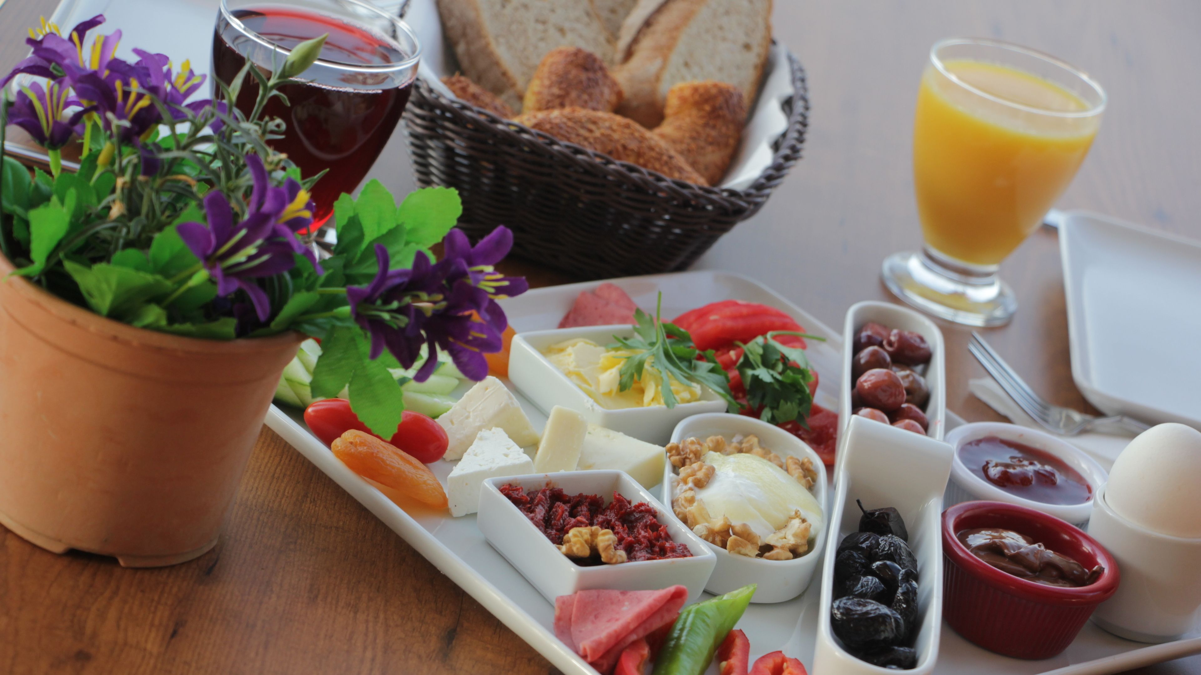Una mesa con una variedad de quesos, frutas, frutos secos y un vaso de zumo de naranja.