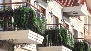 Un edificio con varios balcones, cada uno con tejado de terracota y decorado con plantas florecientes moradas.