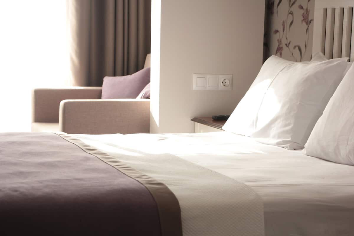 A neatly made bed with white linens, a brown accent pillow, and a headboard with a floral pattern.