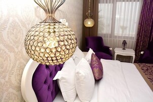 A bedroom with a round, textured light fixture, a tufted headboard, and a purple chair.