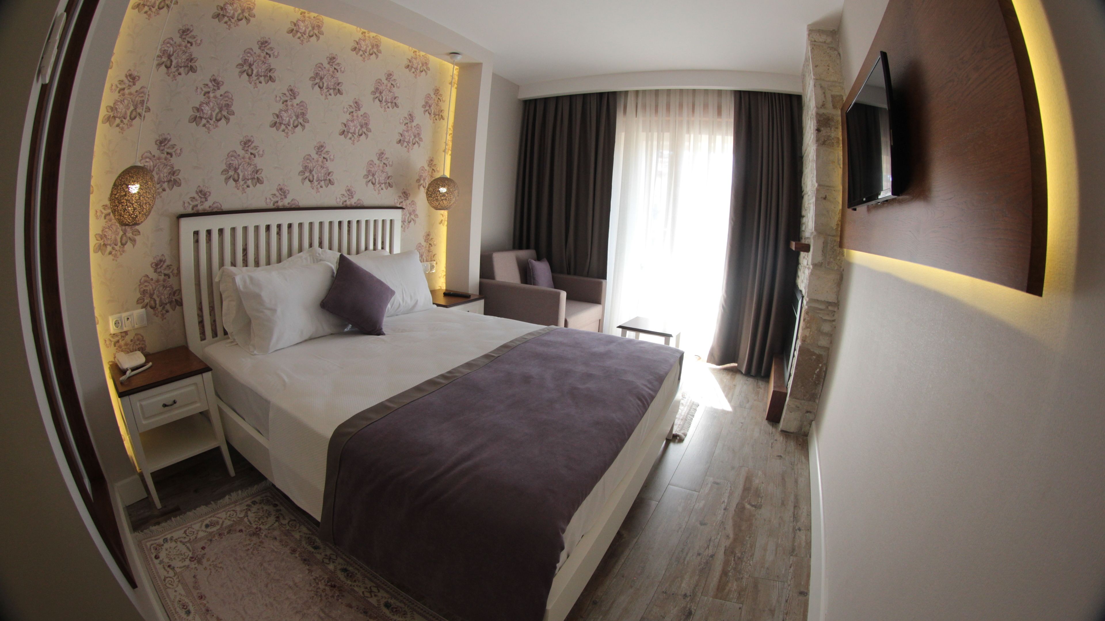 Une chambre d’hôtel avec un grand lit, une table de chevet, une chaise, une télévision et une fenêtre avec des rideaux.