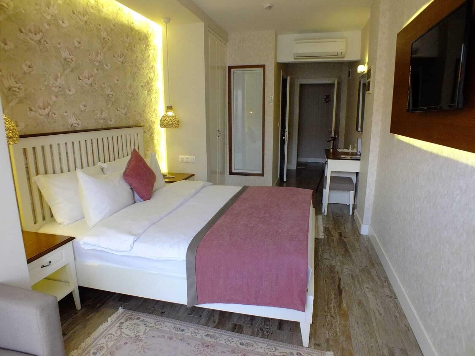 Hotellihuone, jossa on sänky, yöpöytä, lamppu ja peili.