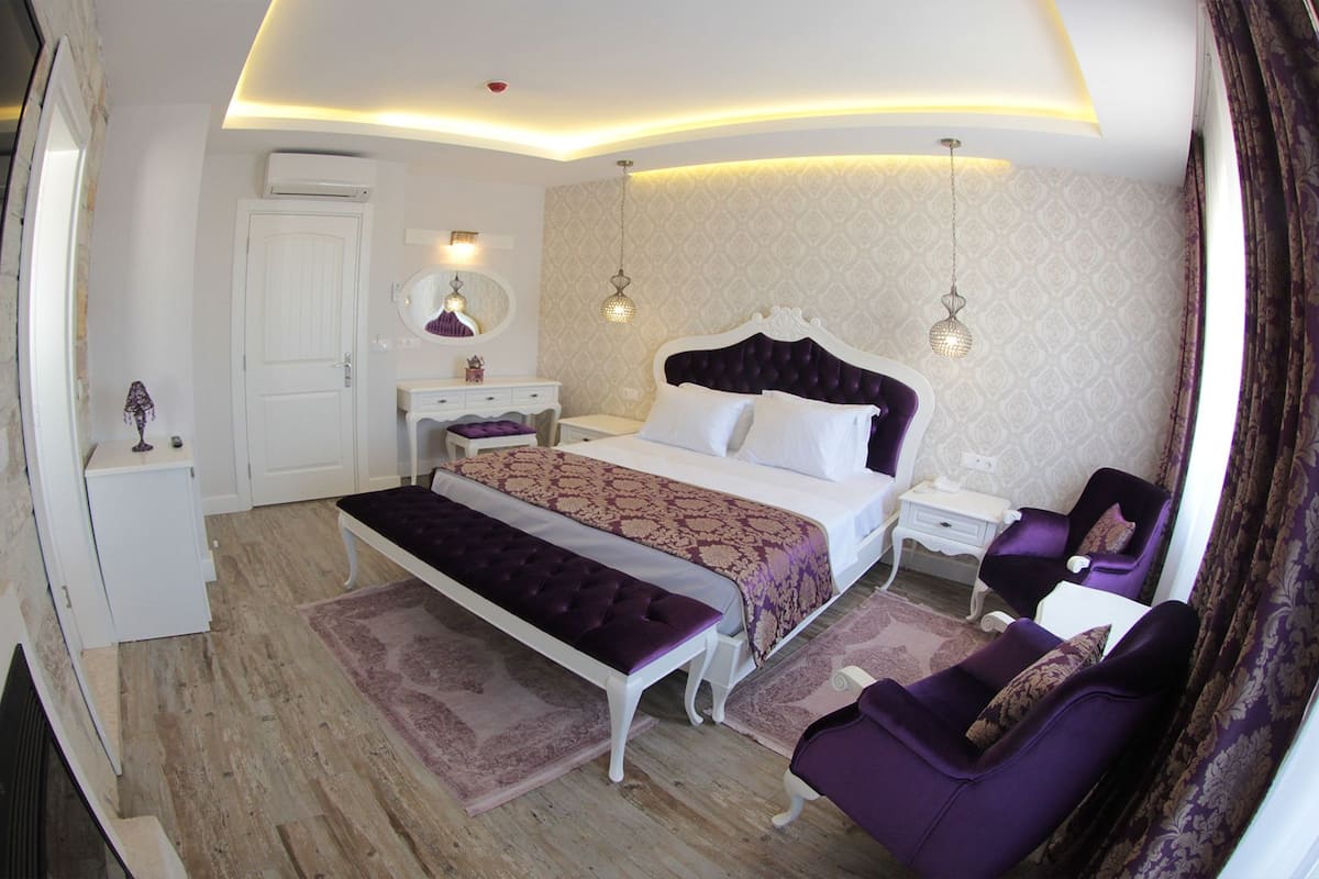A bedroom with a bed, bedside tables, a bench, a chair, and a TV.