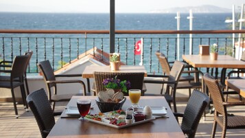 Una mesa de comedor con una bandeja de comida y bebidas, sillas de mimbre y vista al mar.