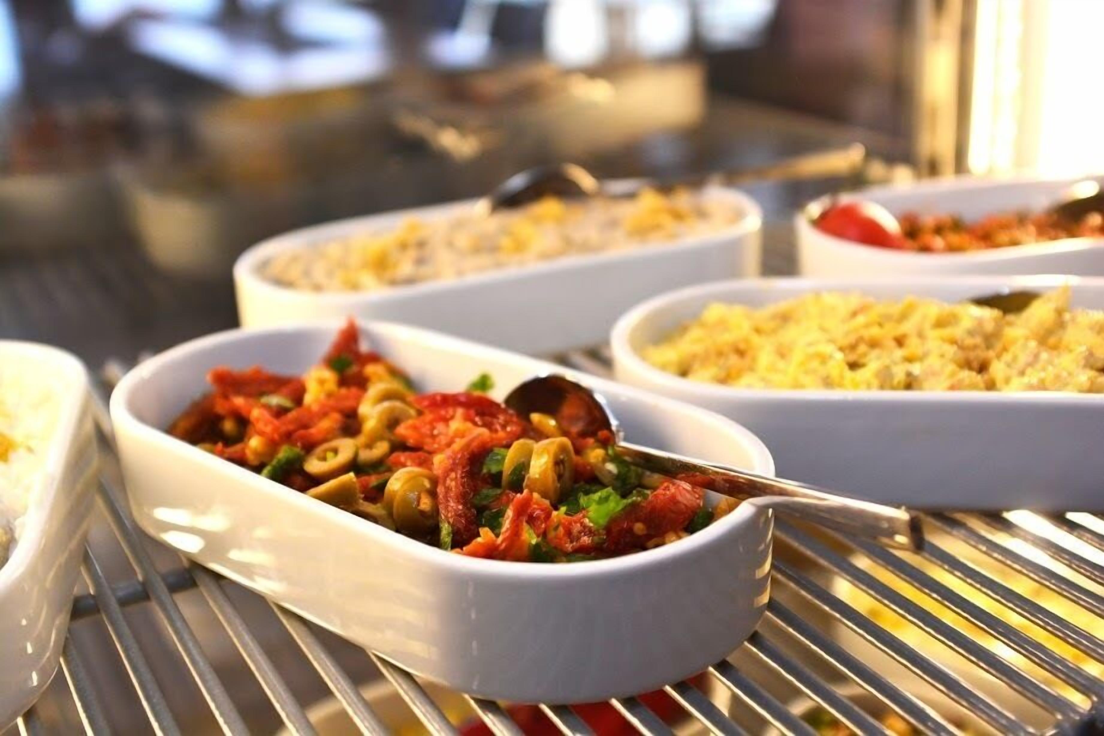 Un bufé con diversos platos, incluyendo un tazón de pasta con verduras y un tazón de arroz.