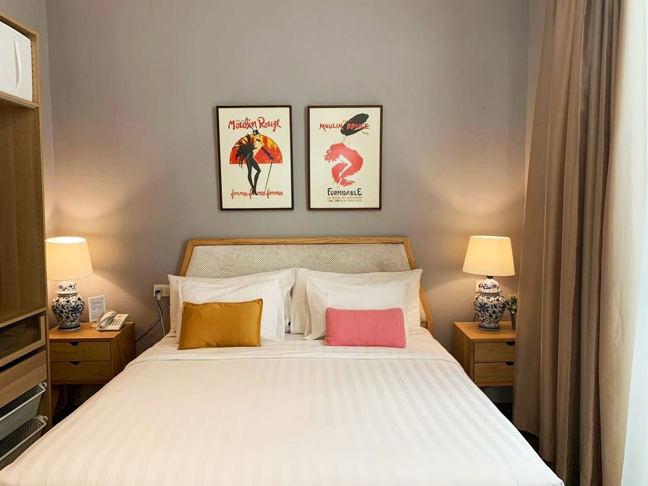 Quarto de hotel com uma cama grande, duas mesas de cabeceira com luminárias e dois cartazes emoldurados na parede.