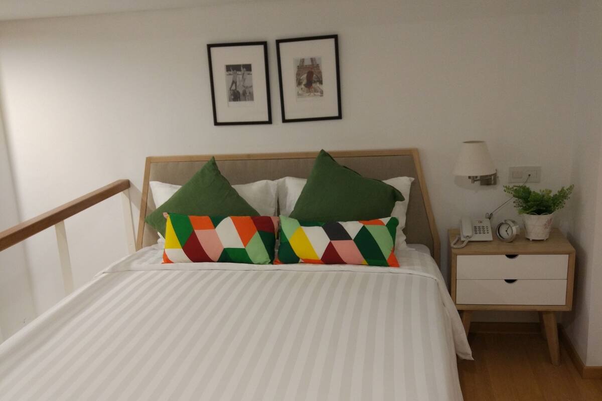 A neatly made bed with striped bedding, a wooden headboard, and colorful geometric pillows.