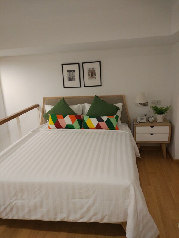 A neatly made bed with striped bedding, a wooden headboard, and colorful geometric pillows. - White Tree Residence (Jakarta)