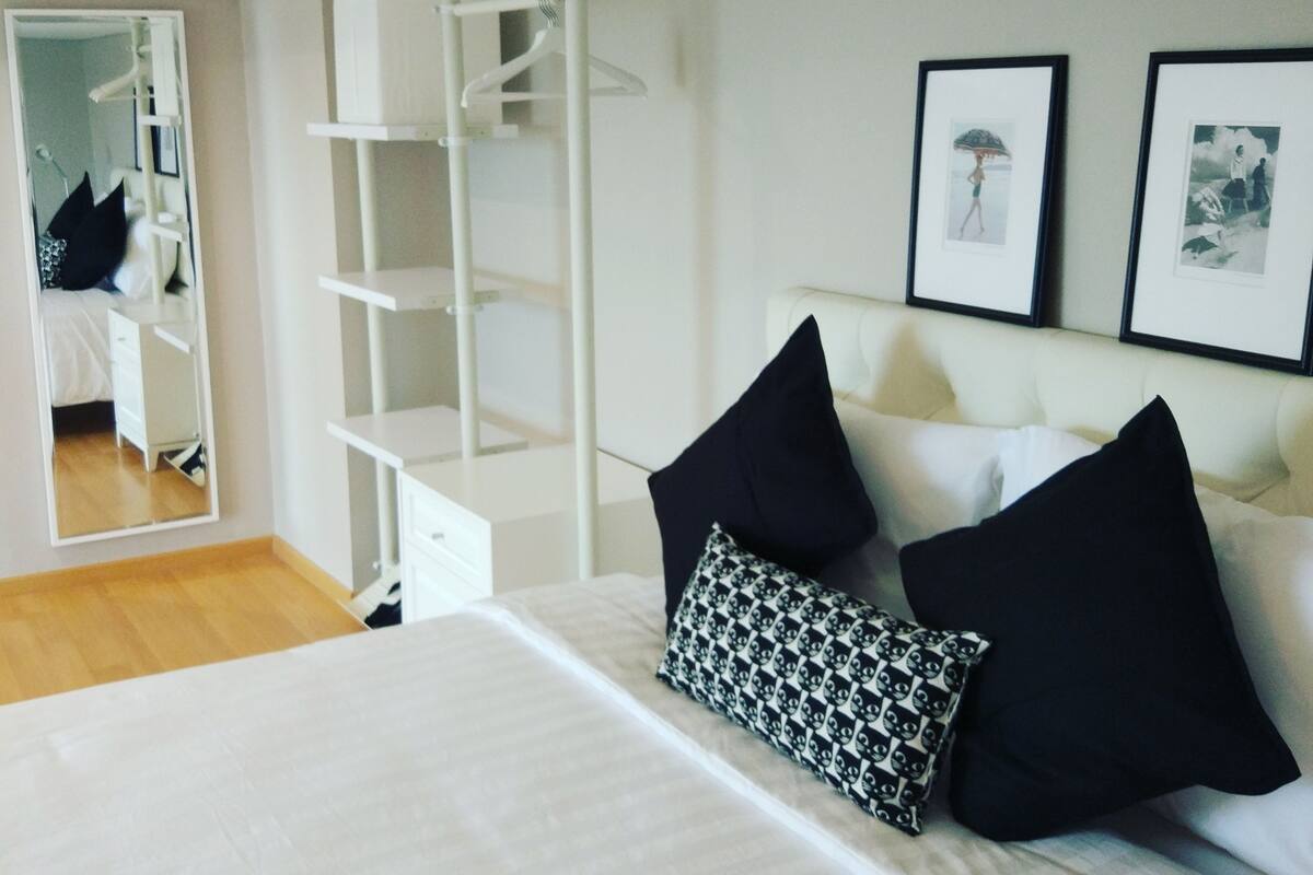 A bedroom with a bed, a white wardrobe, a mirror, and two framed pictures on the wall.