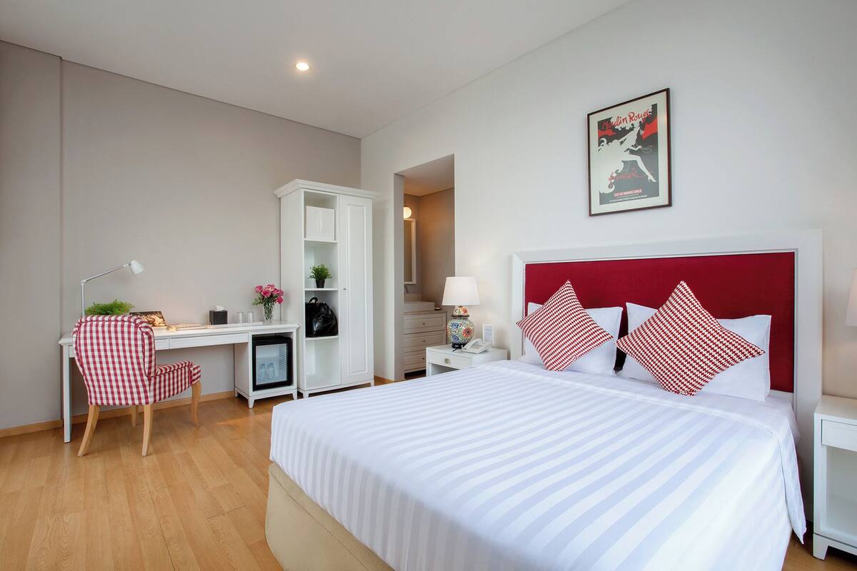 A hotel room with a bed, a desk, a chair, a wardrobe, and a nightstand.