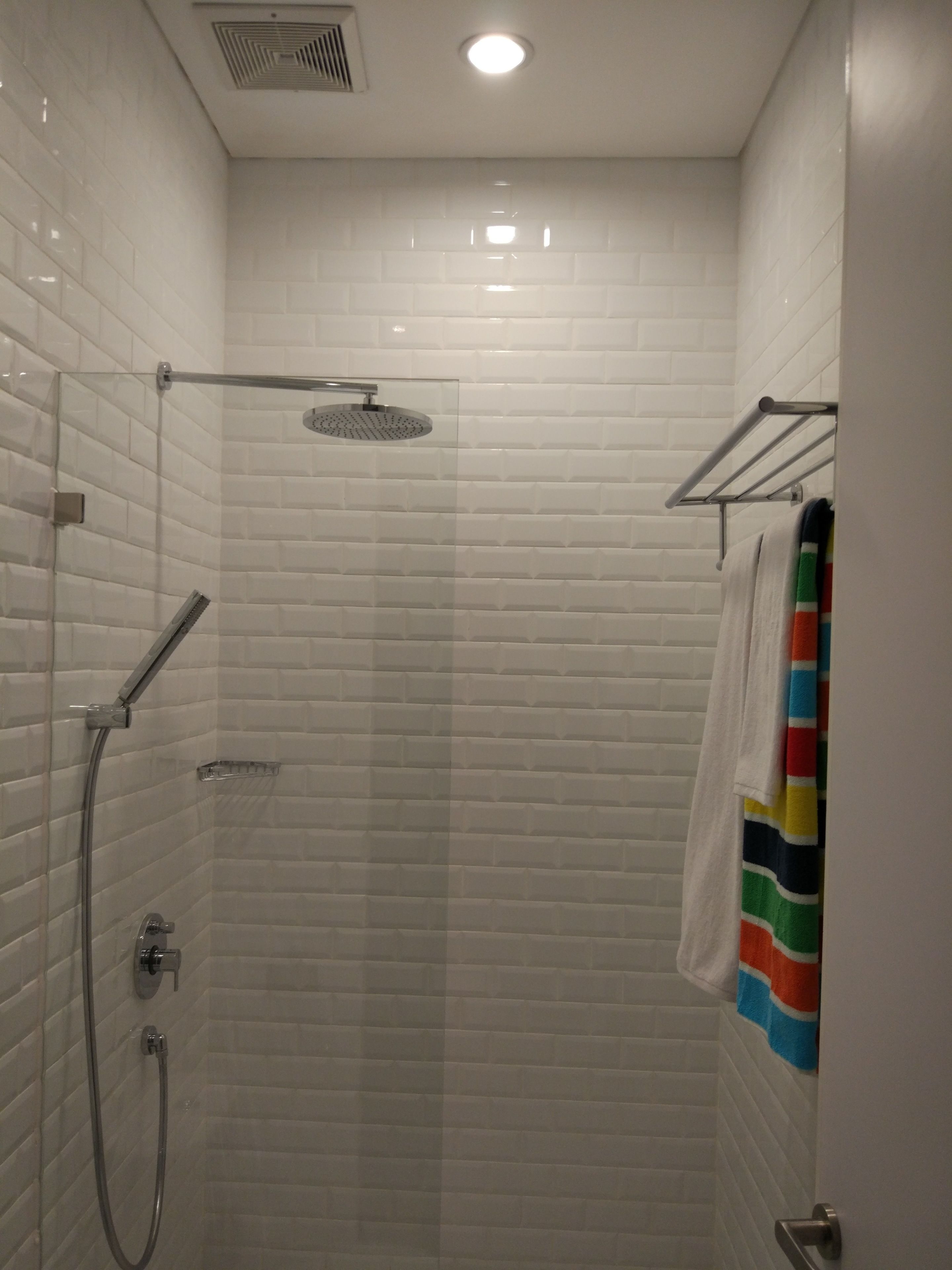 Une douche équipée d’un pommeau de douche à main, d’un pommeau de douche mural en forme de pluie et d’un porte-serviettes avec une serviette à rayures.