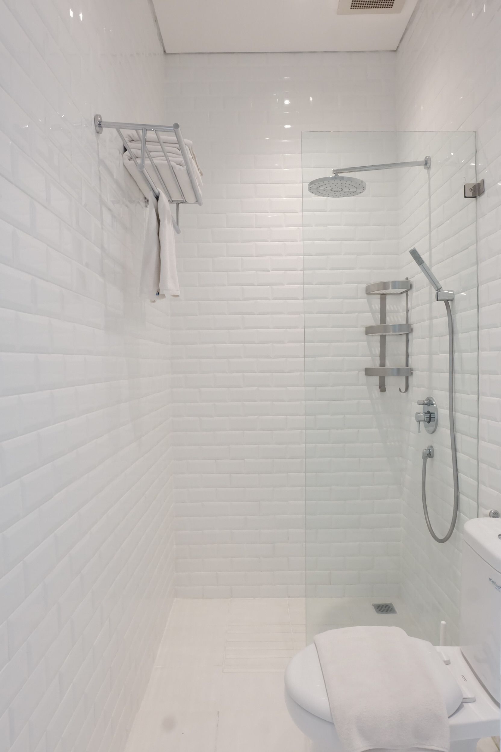 A modern bathroom with white subway tiles, a glass shower enclosure, a white toilet, and a towel rack.