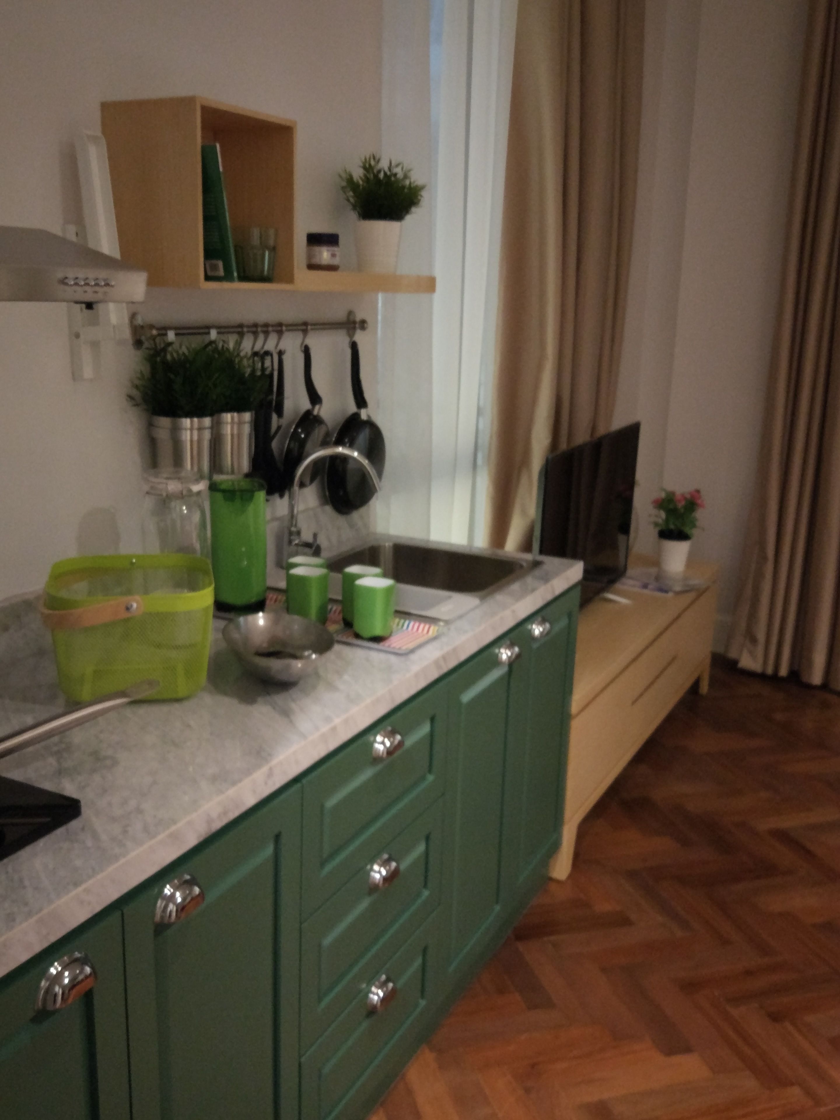 Une cuisine avec des meubles de couleur verte, un plan de travail en marbre et un plancher en bois.