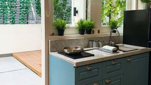 A modern kitchen with a large window, a black refrigerator, and a countertop with a frying pan and a kettle. - White Tree Residence (Jakarta)